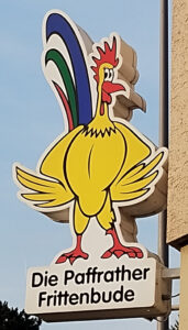 Das Logo der Paffrather Frittenbude als Leuchtreklame an der Hauswand des Geschäfts.